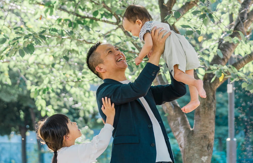 木の下で子どもを抱き上げる中西勇太